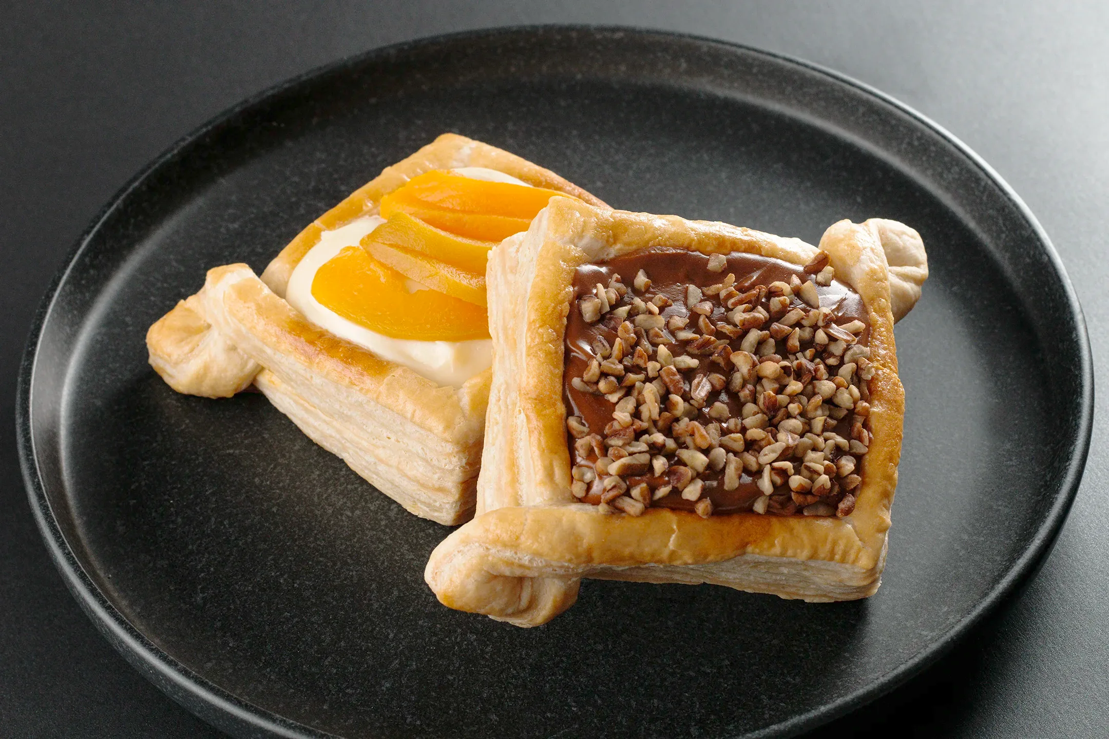 Fotografía gastronómica de postres de hojaldre rellenos de crema pastelera con duraznos y dulce de leche con nueces.
