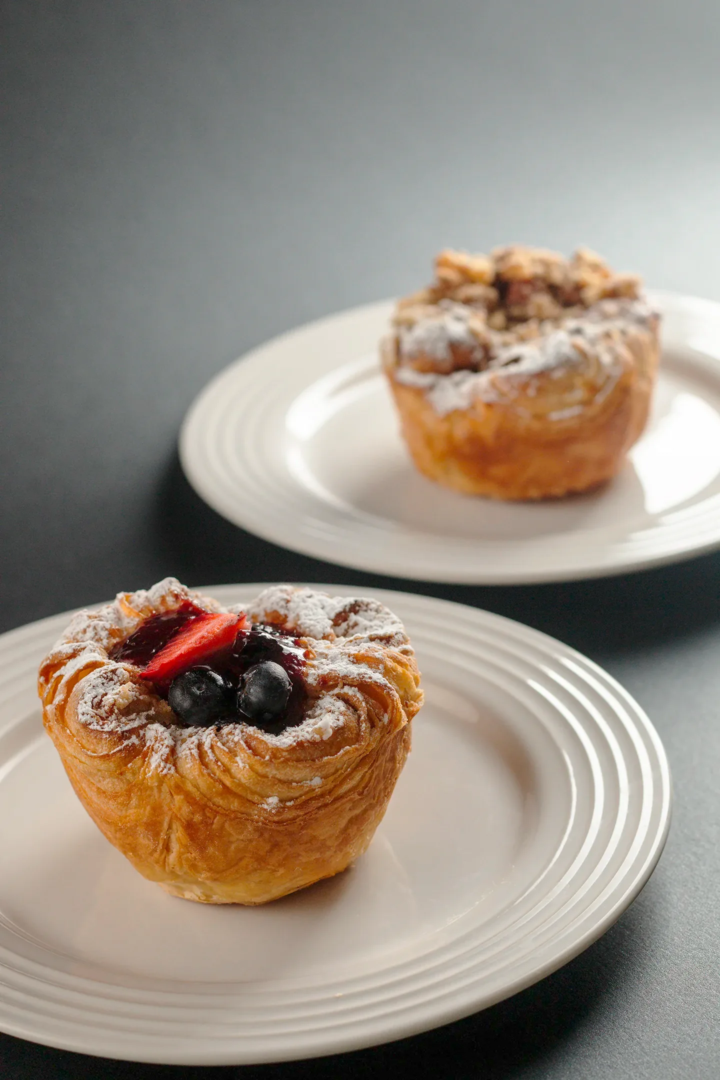Exquisitos postres de hojaldre con frutos rojos y nueces caramelizadas, resaltados en un fondo oscuro, imagen profesional de repostería en Chihuahua.