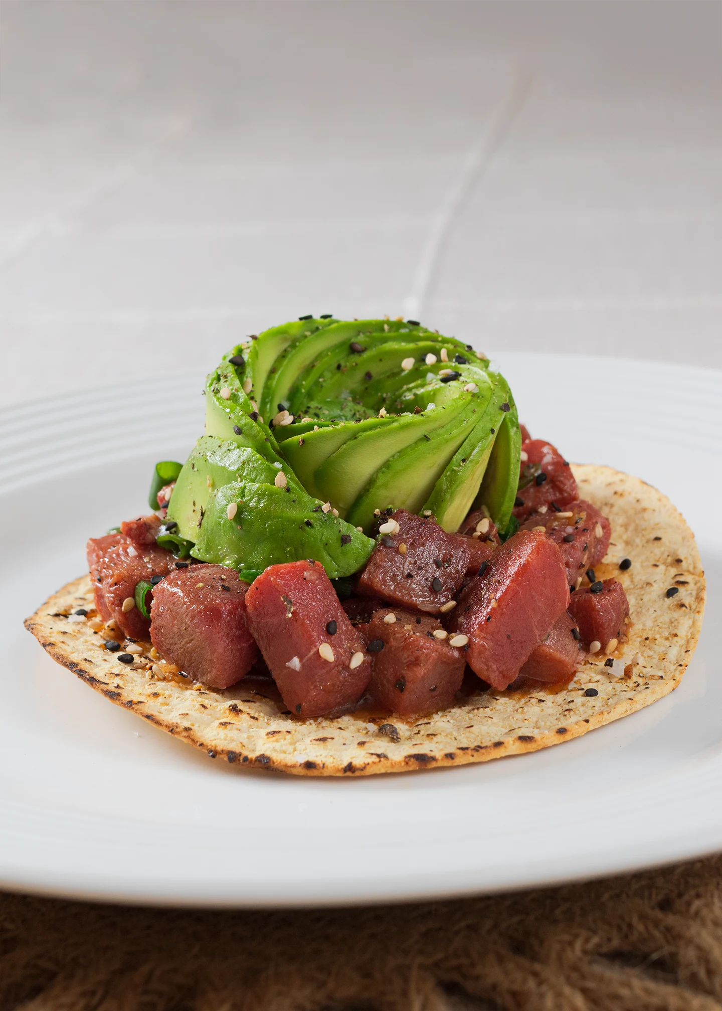 Fotografía gastronómica de una Tostada crujiente con cubos de atún marinado, decorada con una flor de aguacate.