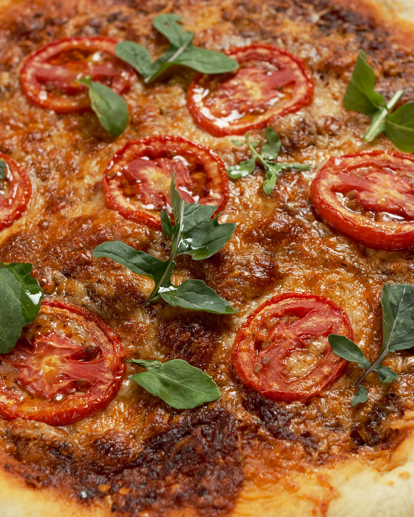 Detalle de pizza artesanal con rodajas de tomate fresco, queso gratinado y hojas de arúgula, capturada en una toma cercana que resalta la textura y el brillo de los ingredientes.