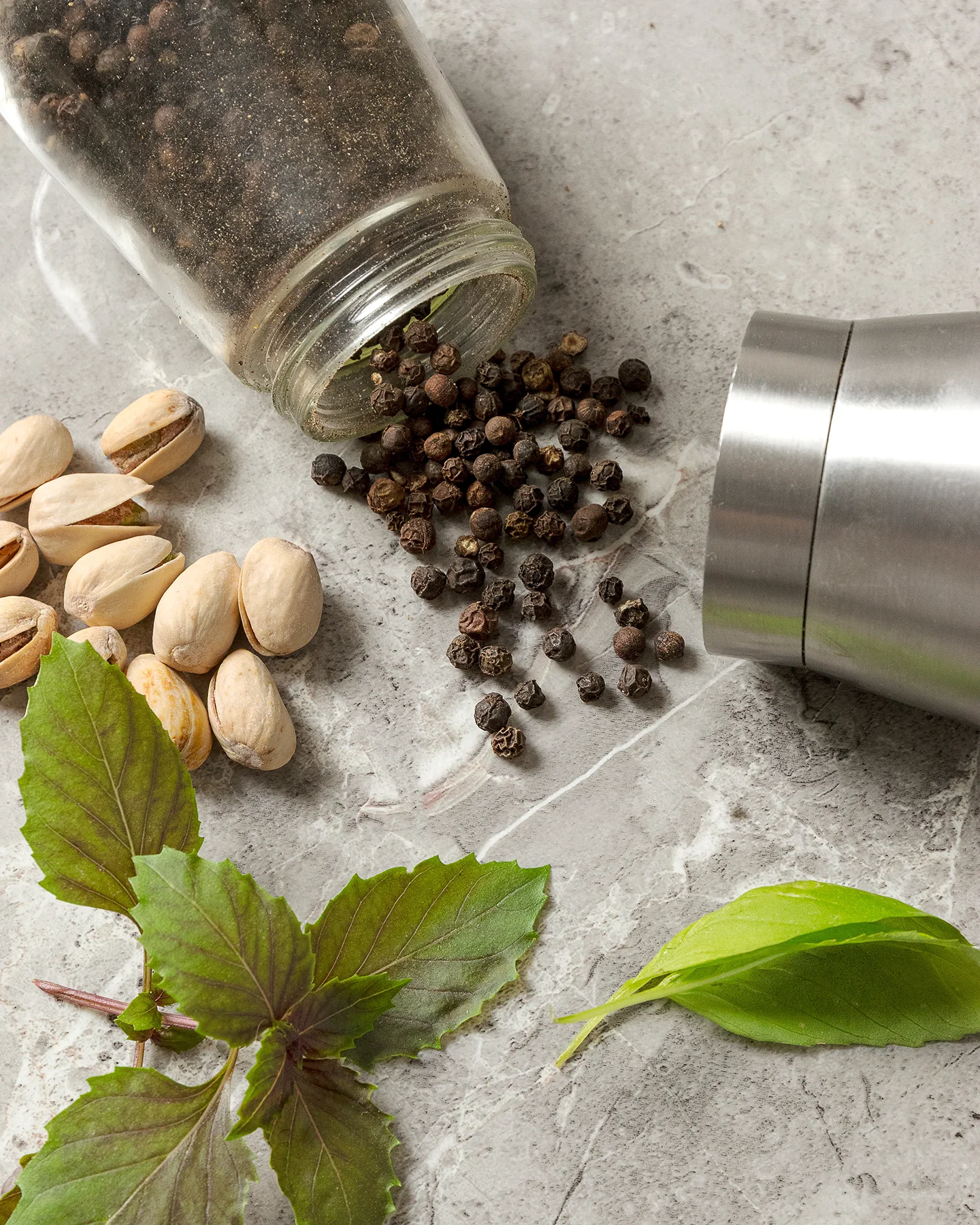 Granos de pimienta negra con pistaches y hojas de albahaca, sobre mármol. Fotografía de especias y producto.