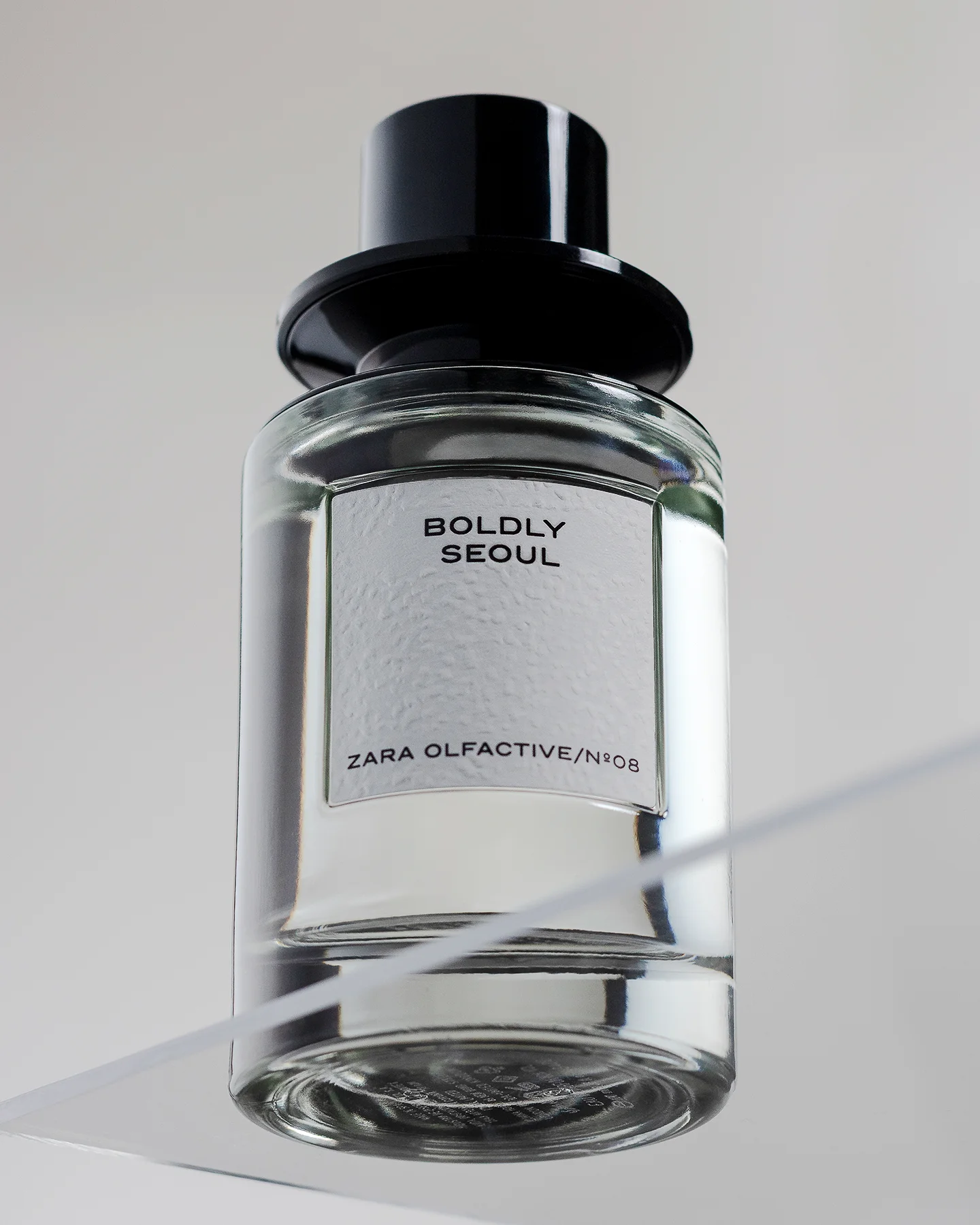 Fotografía de un perfume Zara Olfactive Nº08 Boldly Seoul sobre una base de acrílico transparente, con fondo gris claro. Imagen con iluminación limpia y estilo minimalista, ideal para publicidad de producto. Fotografía realizada en Chihuahua, México.
