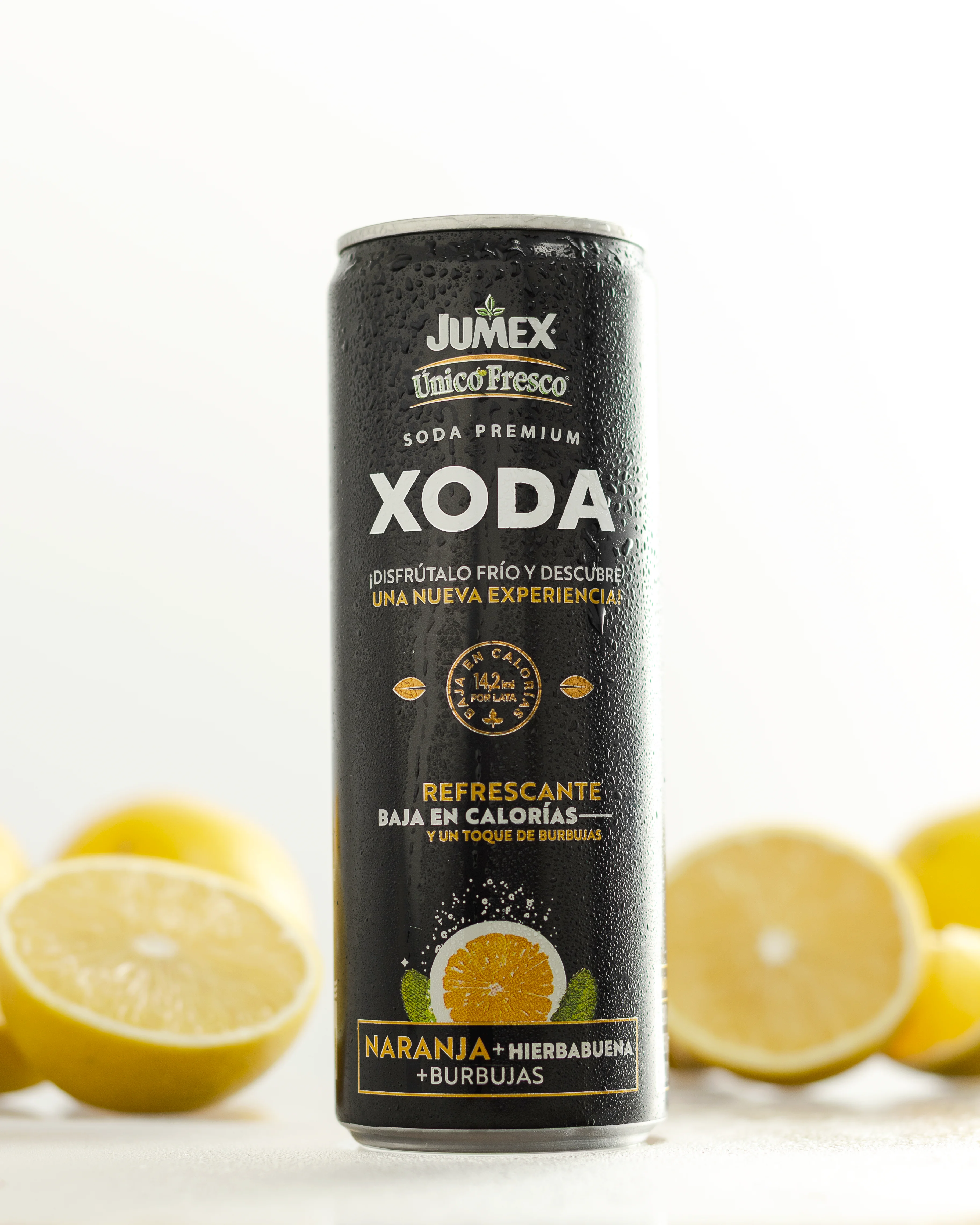 Fotografía de producto con cítricos de una lata de refresco Jumex Xoda Naranja + Hierbabuena con condensación, sobre fondo blanco.