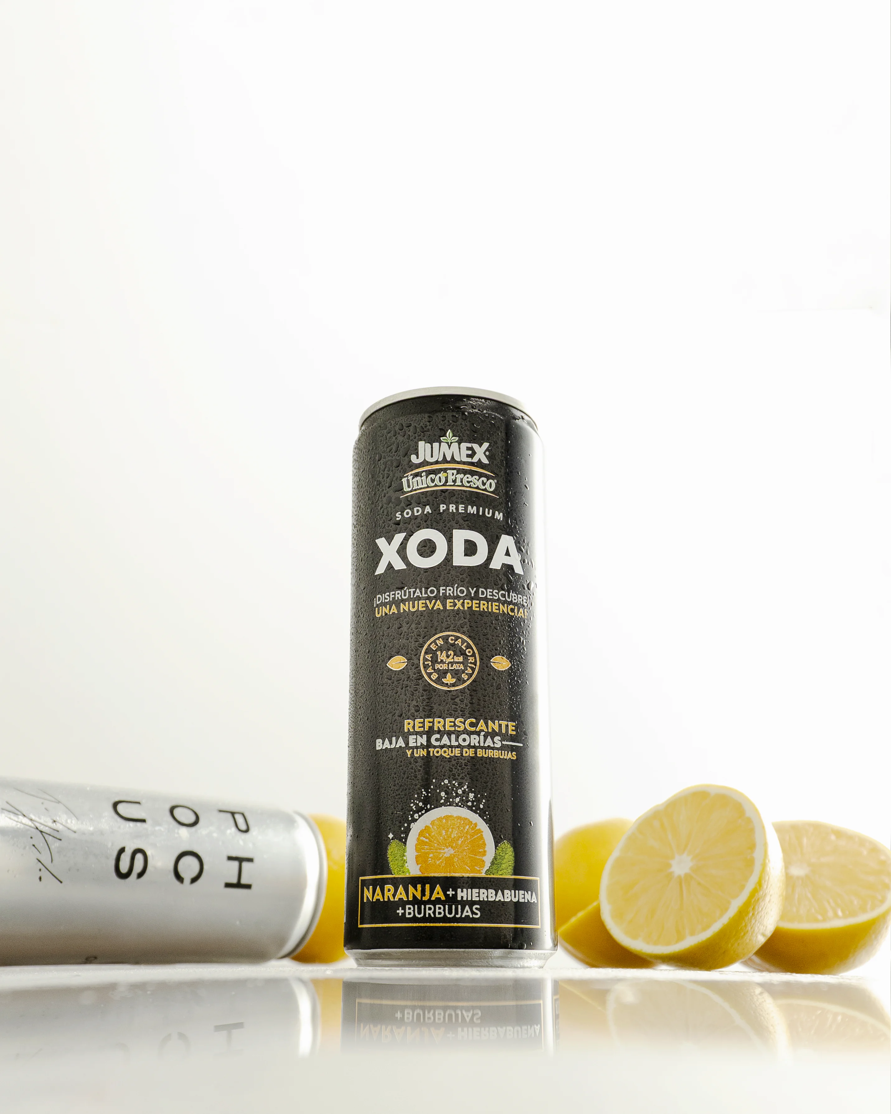 Fotografía de Estudio de Producto en Chihuahua de una Lata de refresco Jumex Xoda en plano general con un reflejo y naranjas, con fondo blanco luminoso.