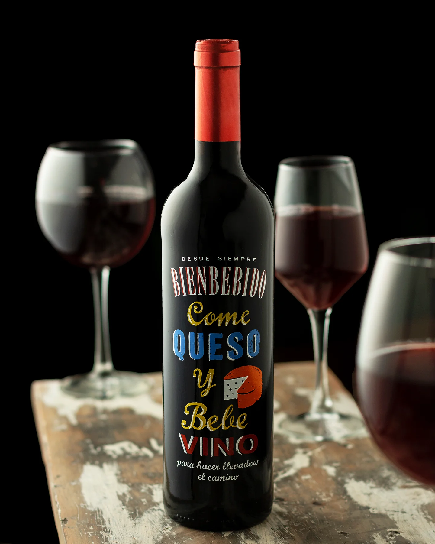 Fotografía gastronómica de botella de vino tinto con copas de cristal en segundo plano, fondo negro y luz suave, pensada para publicidad y contenido comercial.