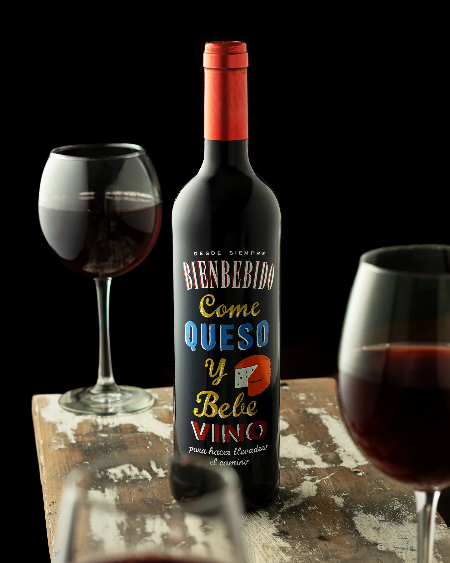 Fotografía de producto de botella de vino tinto sobre mesa de madera rústica, con iluminación cinematográfica y composición minimalista para uso publicitario.