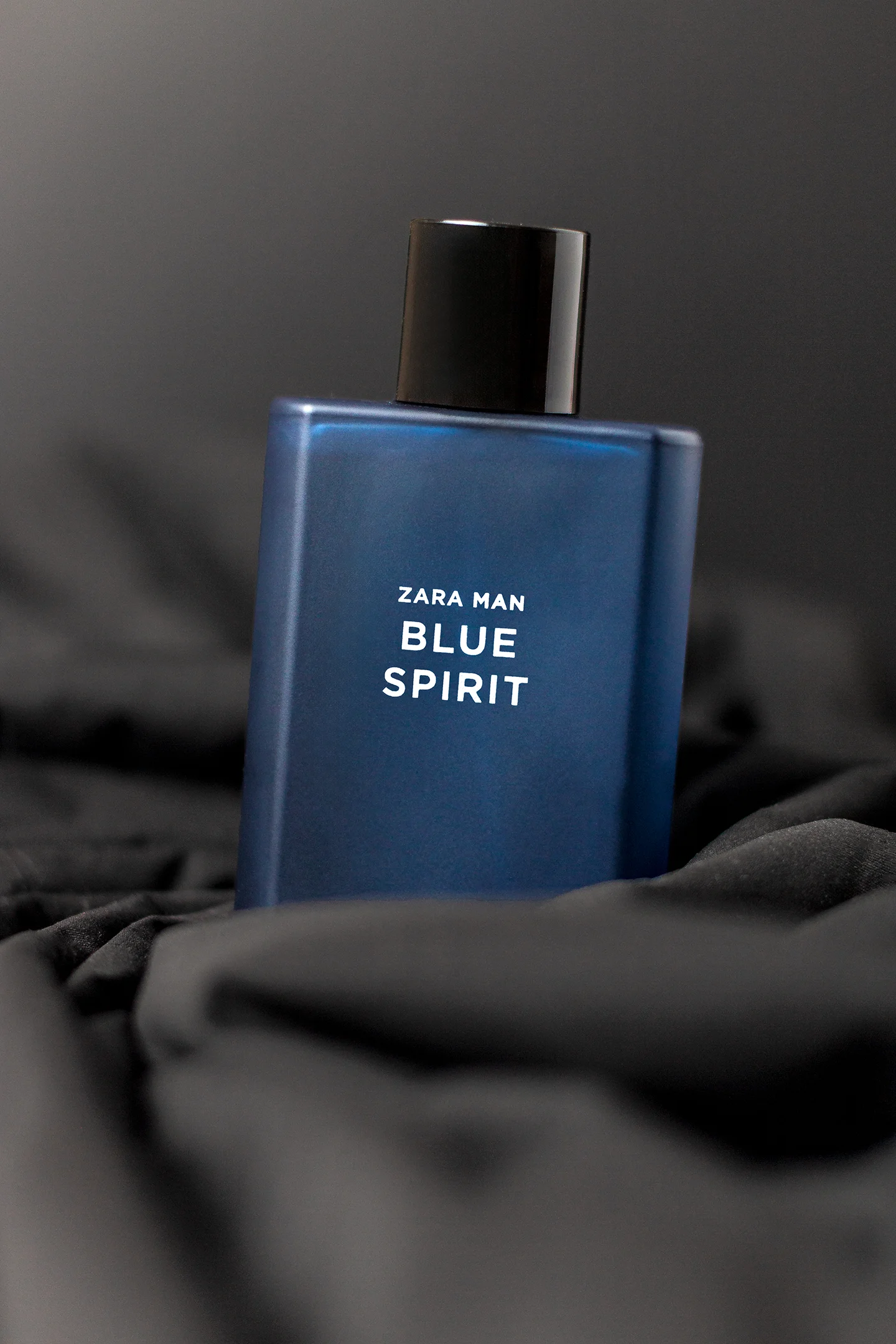 Perfume Zara Man Blue Spirit de envase azul mate con tapa negra, sobre fondo de tela negra, fotografía de producto profesional por Andres Gardea.