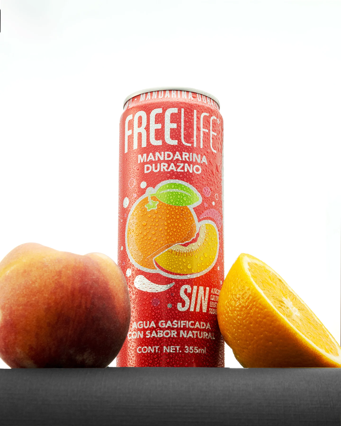 Toma contrapicada publicitaria de lata helada de Freelife Mandarina Durazno de frente, mostrando durazno entero y media naranja sobre base negra y fondo blanco puro.