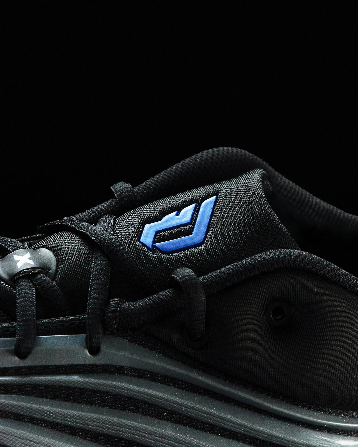 Primer plano de la lengüeta de tenis Adidas de tela de malla negra, centrada en el logo de Adidas 'Performance' bordado en azul eléctrico brillante y agujetas negras texturizadas.