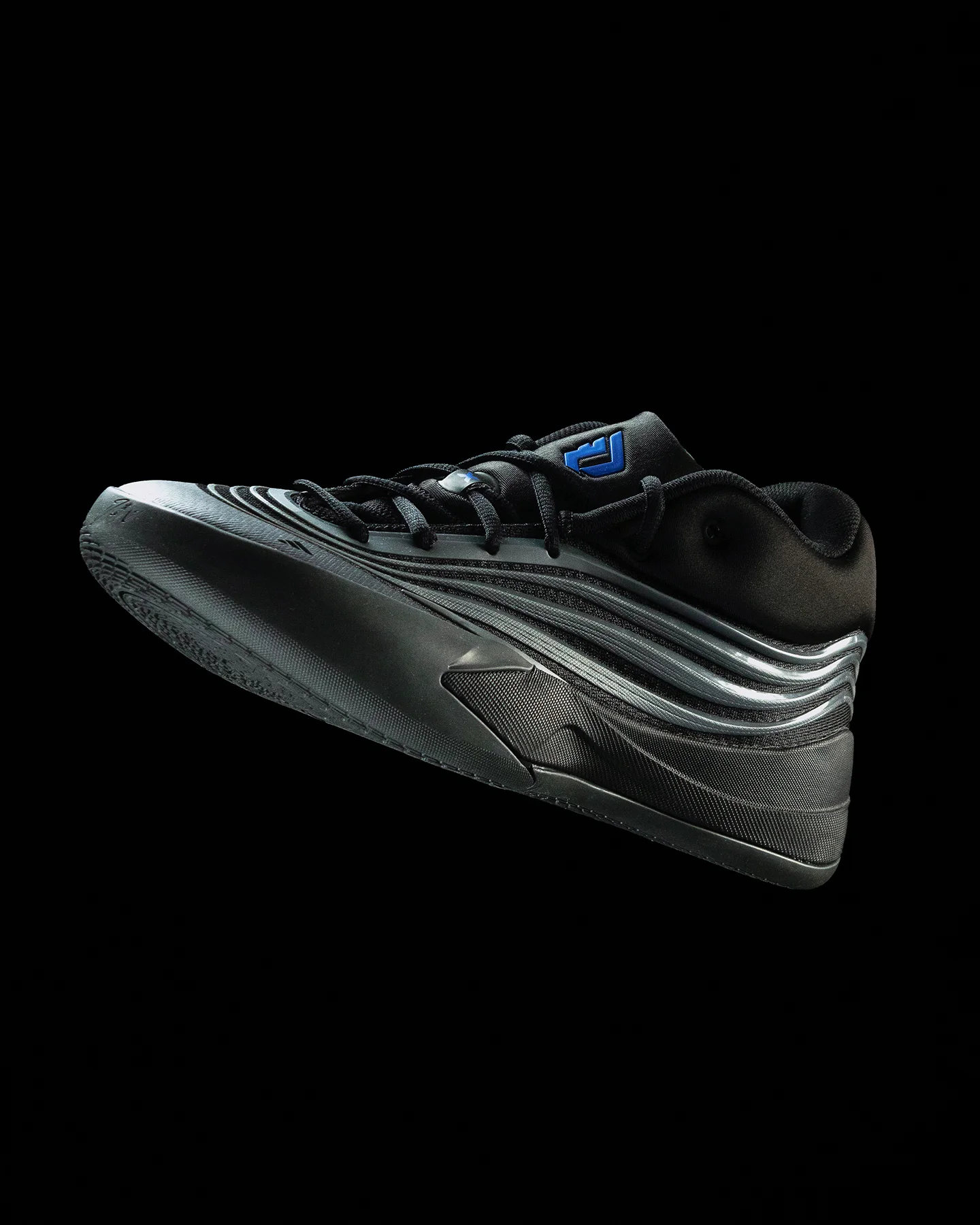 Fotografía de producto de tenis Adidas negros y grises flotando en ángulo lateral sobre fondo negro, mostrando diseño futurista de líneas fluidas y logo Adidas azul en la lengüeta.