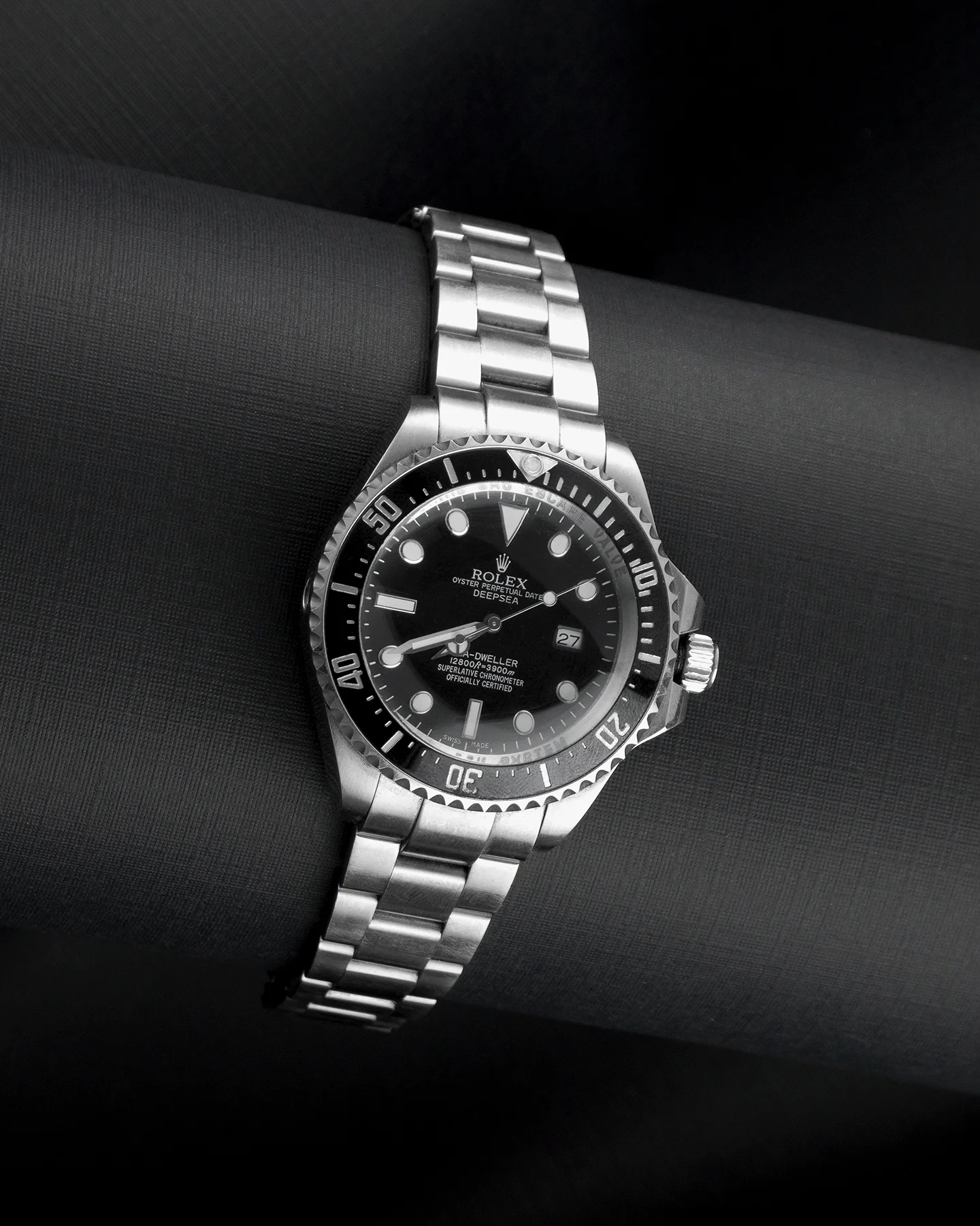 Fotografía de producto de lujo en primer plano de reloj Rolex Oyster Perpetual Date Deepsea de acero inoxidable sobre fondo negro texturizado y mate.
