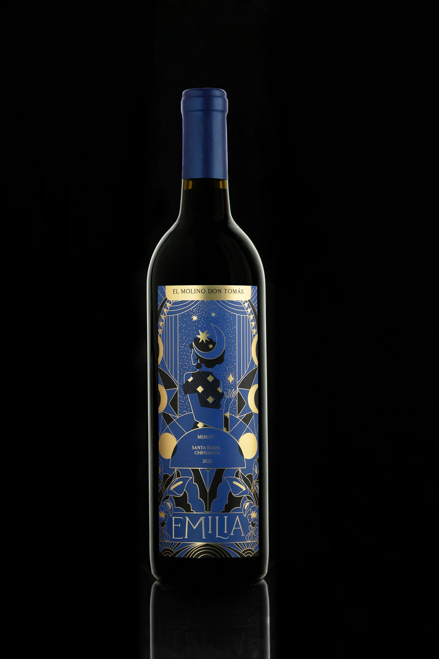 Fotografía de producto elegante de botella de vino Merlot 'Emilia' de El Molino Don Tomás (Santa Isabel, Chihuahua) con etiqueta azul y dorada de diseño celestial y reflejo en la base, sobre fondo negro.