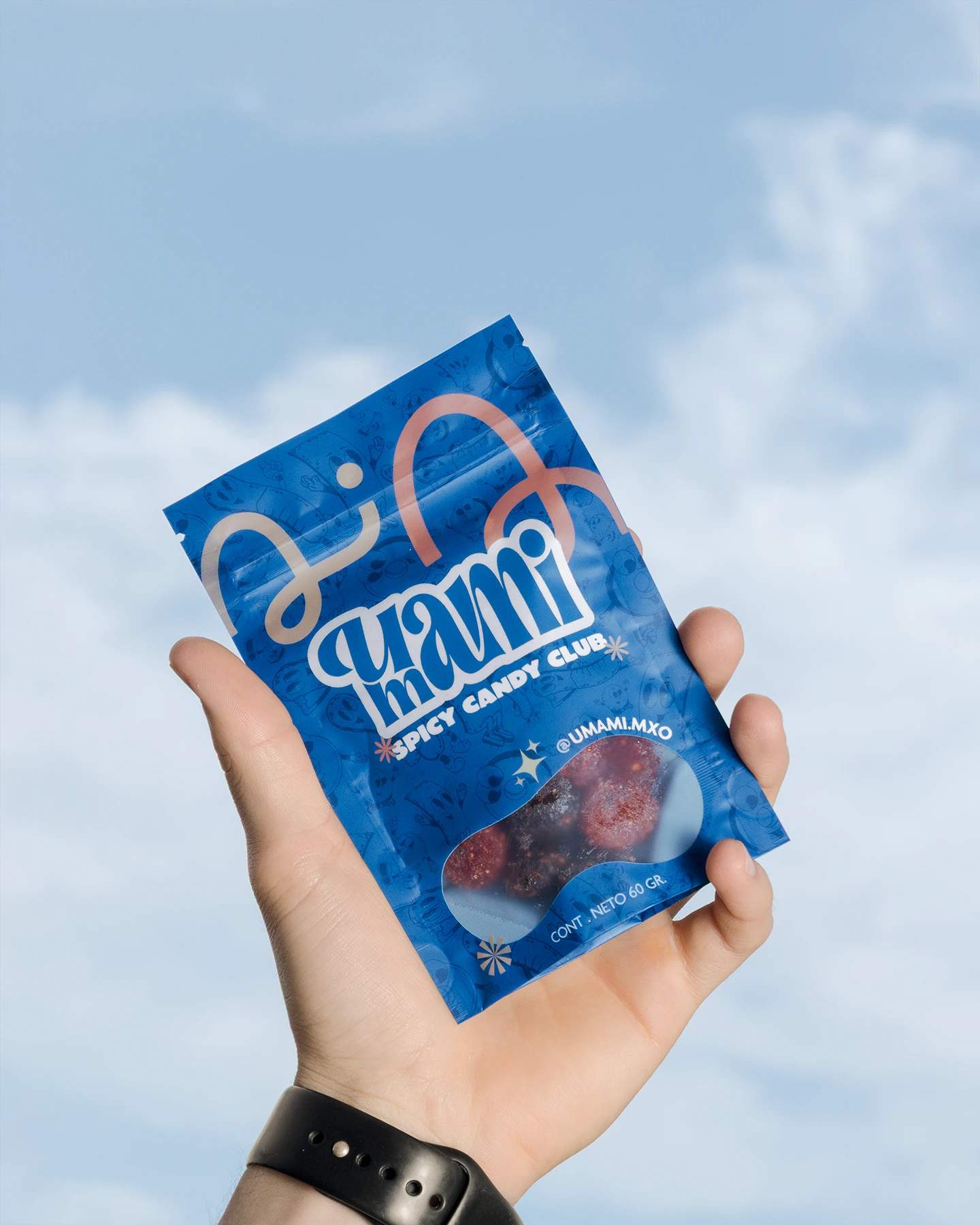 Mano sosteniendo empaque de dulces picantes en primer plano sobre fondo de cielo azul despejado.